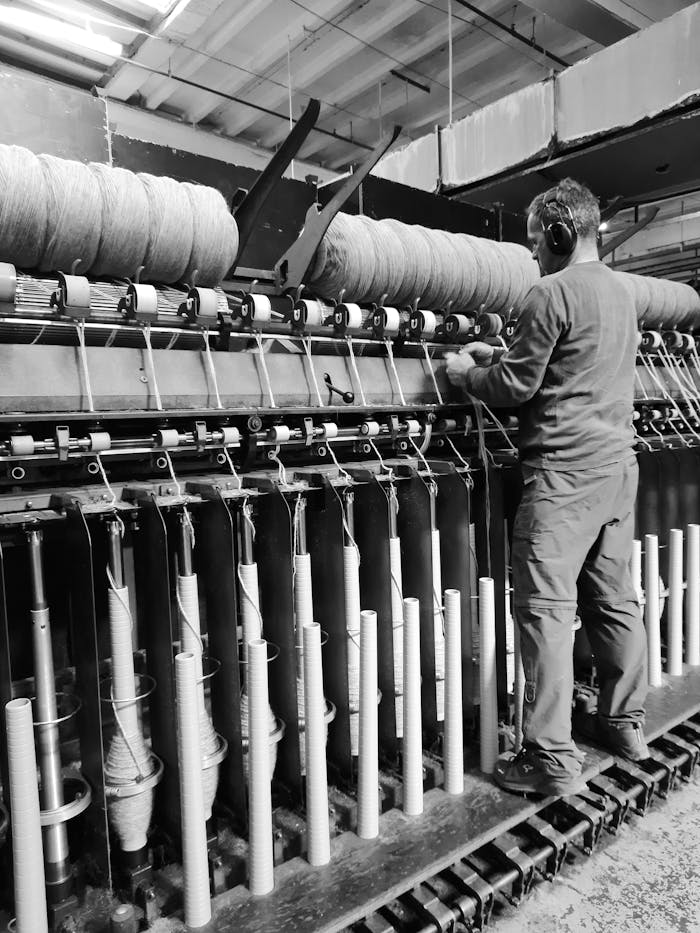 A man working with industrial machinery in a factory setting. Black and white image.