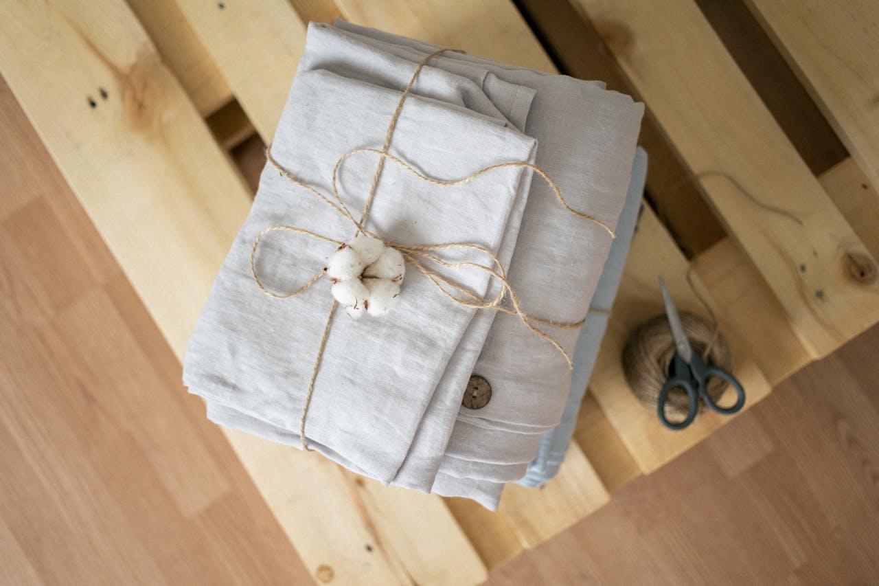 Top view of neatly folded linen fabric tied with twine on a wooden pallet, evoking natural simplicity.