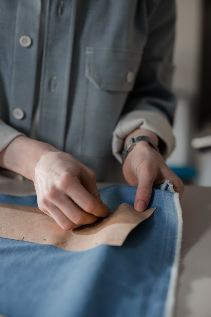 Hands meticulously working on a sewing pattern on blue fabric, showcasing dressmaking skills.